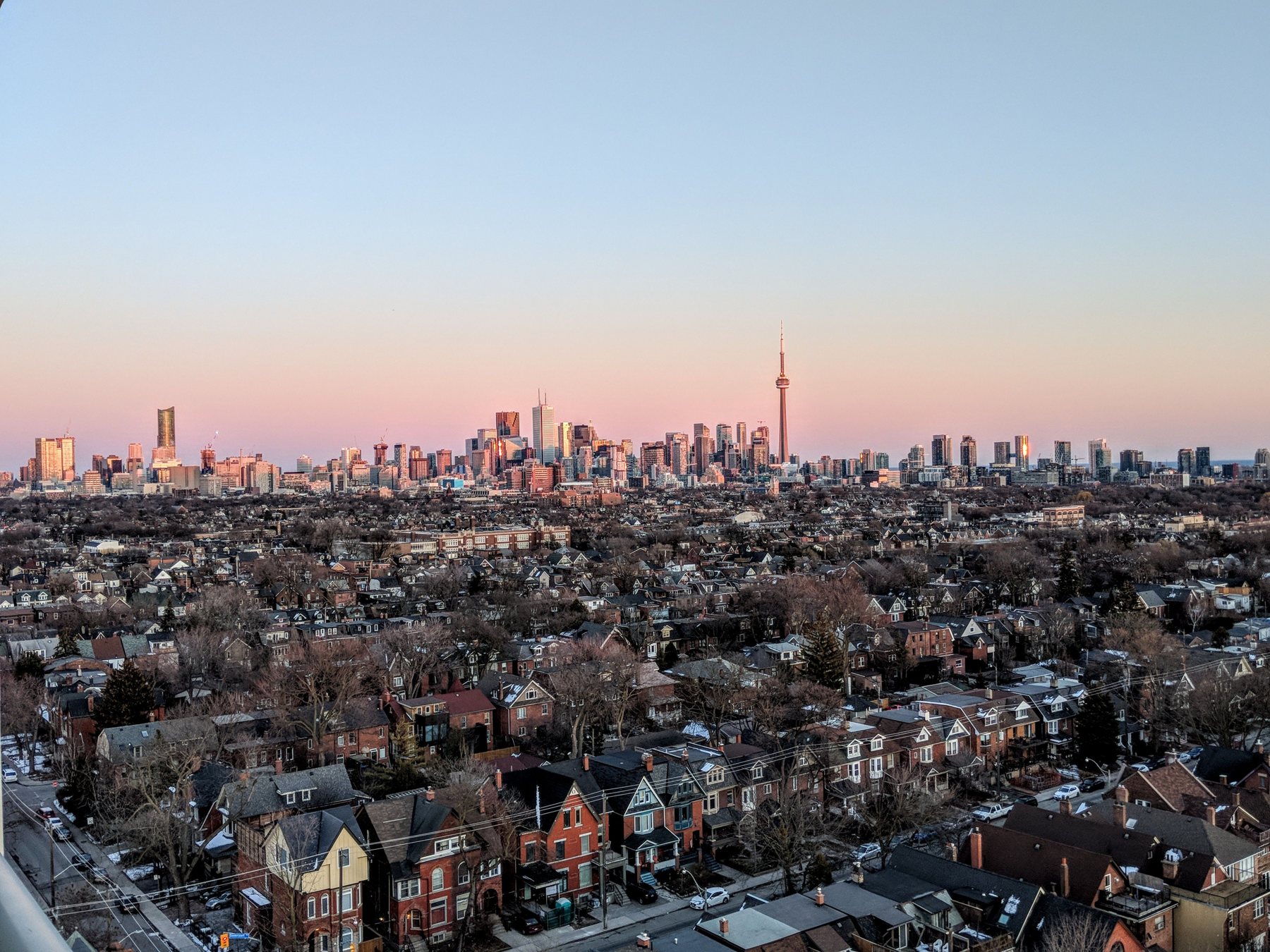 The Toronto skyline at sunset, seen over rows of houses